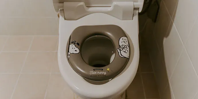 白い洋式便器に、スヌーピーのイラストが描かれたグレーの補助便座がセットされています。