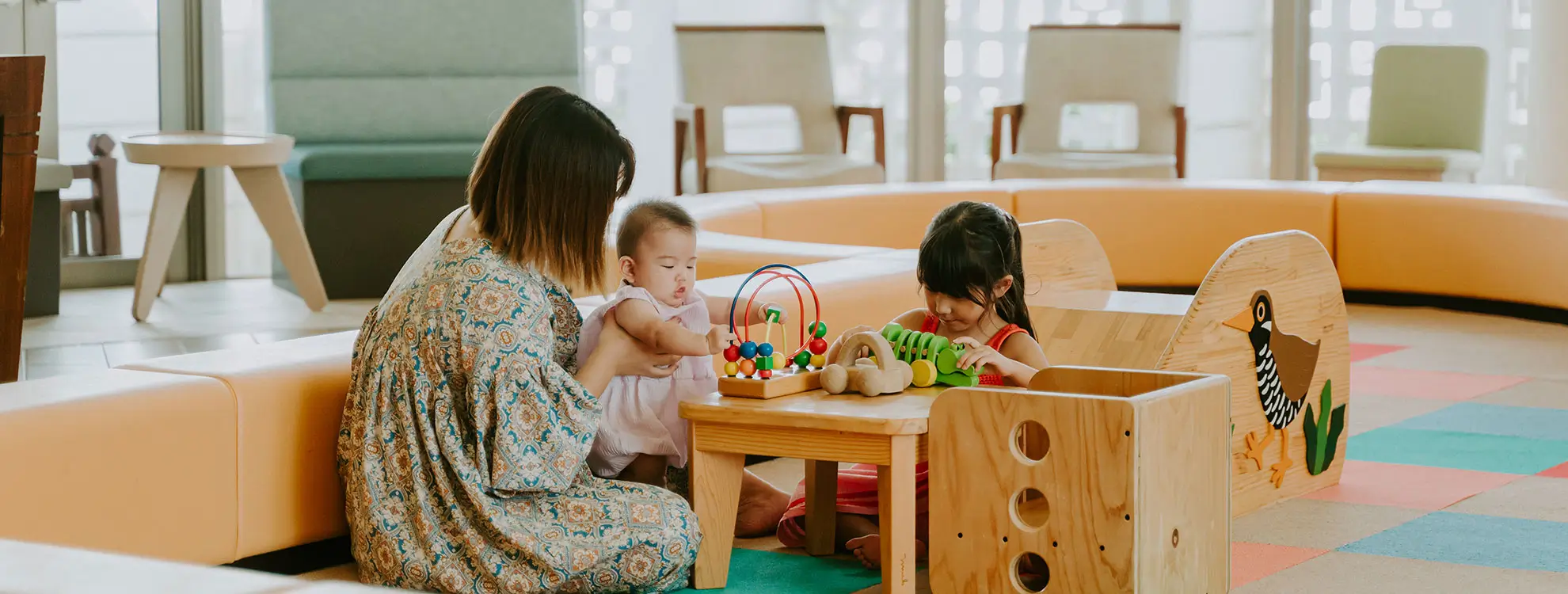 ホテルロビーの一角で、親子が温かみのある木製の知育玩具を使って楽しそうに遊んでいます。