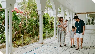 白いアーチが連なる回廊を、子連れの家族が緑豊かな中庭を眺めながら穏やかな足取りで歩いています。