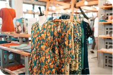 深緑の地にオレンジの花柄が描かれたワンピースが、金属製のハンガーラックに吊るされています。