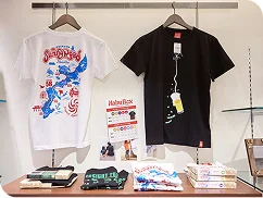 沖縄の地図が描かれた白とビール柄の黒のTシャツが、ハンガーに吊るされ棚に並んでいます。