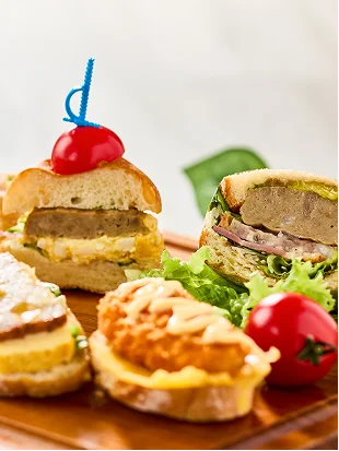 青いピックを刺したミニバーガーやサンドイッチが、瑞々しいトマトとレタスと共に木製のプレートへ並んでいます。