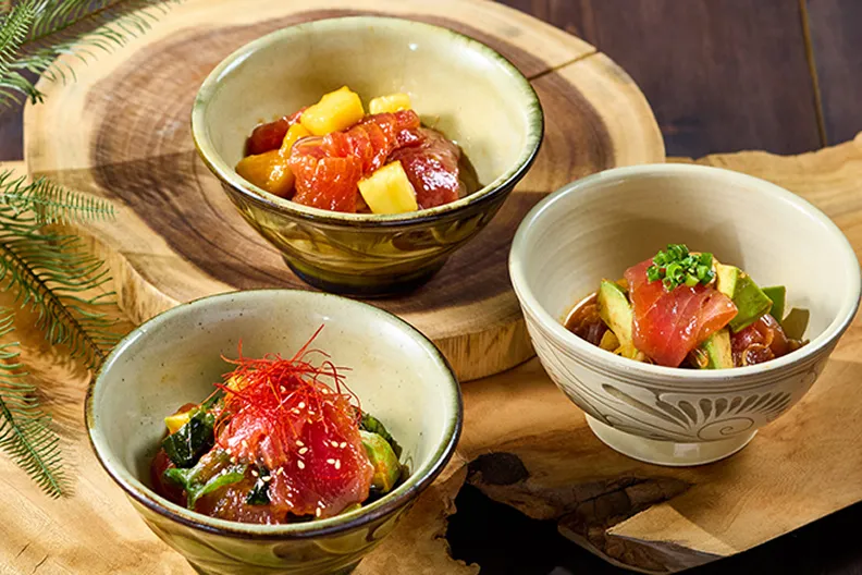 不規則な輪郭の切り株プレートの上に、マグロとアボカドを和えたポキ丼が盛られた淡いベージュの小鉢が三つ並んでいます。