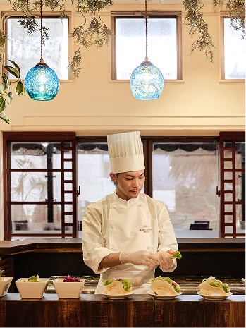 白いシェフ帽の料理人が、ライブキッチンで沖縄料理の進化系お好みタコスを丁寧に盛り付けています。