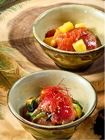 淡い緑色の陶器鉢に盛られた新鮮なマグロのポキ丼が、年輪が浮かぶ素朴な木製台の上に並んでいます。