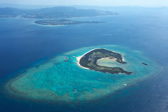 鮮やかなエメラルドグリーンの浅瀬に囲まれた島が浮かび、その奥に瀬底島と本部半島を遠望できます。